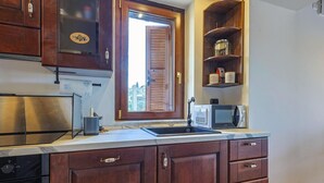 A kitchen with wooden cabinets, a stainless steel refrigerator, a microwave, and a window with a view. - DAD House by Rentbeat (Fastello - Frazione Viterbo)