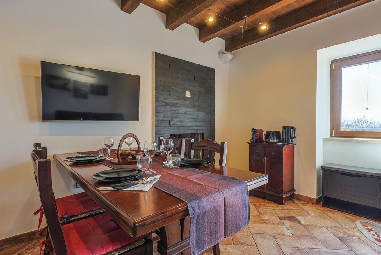 Un coin repas avec une table en bois dressée pour quatre personnes, un téléviseur à écran plat fixé au mur, une cheminée en pierre et une fenêtre offrant une vue agréable.