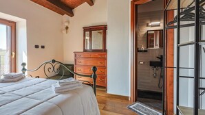 A bedroom with a bed, wooden dresser, and a bathroom visible through an open door. - DAD House by Rentbeat (Fastello - Frazione Viterbo)
