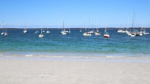Ein Strand mit zahlreichen Segelbooten, die in ruhigem Wasser vor Anker liegen.