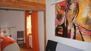 Un dormitorio con cama, una silla, un cuadro y una cortina naranja.