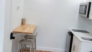 Una cocina compacta con una mesa de madera, dos taburetes, un microondas y armarios blancos.