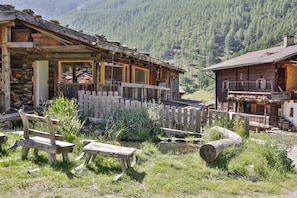 Un rustico chalet di legno con un balcone, una piccola panca in legno e un tronco in primo piano.