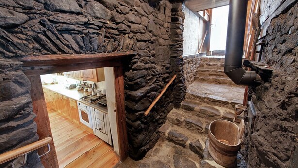 Interior de parets de pedra amb una escala de fusta, una zona de cuina i una llar de foc.