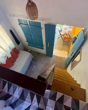 A bedroom with a bed, a blue wardrobe, a window with curtains, and a staircase leading to a dining area. - Praia do Sagi (Baía Formosa)