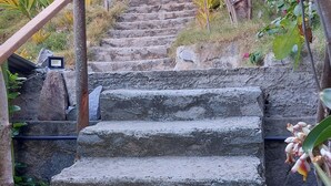A stone staircase leading up to a building, surrounded by greenery and a metal railing. - Praia do Sagi (Baía Formosa)
