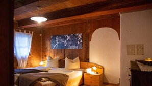 Una habitación con piso de madera, una cama, una mesita de noche y un televisor montado en la pared.