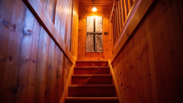 Una escalera de madera que lleva a una puerta con un diseño de cruz, rodeada de paredes de madera.