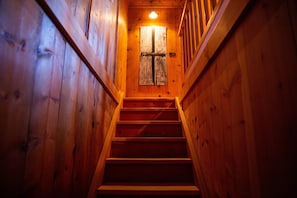 Un escalier en bois mène à une porte ornée d’une croix, le tout étant entouré de murs en bois.