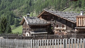 Una cabaña de madera con techo inclinado, rodeada por una valla de madera, con montañas al fondo.