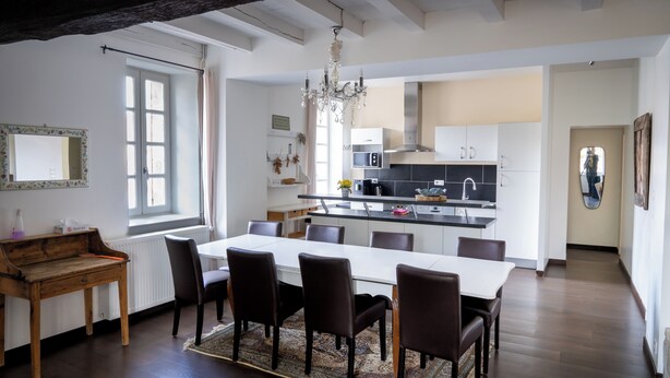 Une cuisine moderne avec des meubles blancs, un îlot central et un coin repas comprenant une table et des chaises en bois.