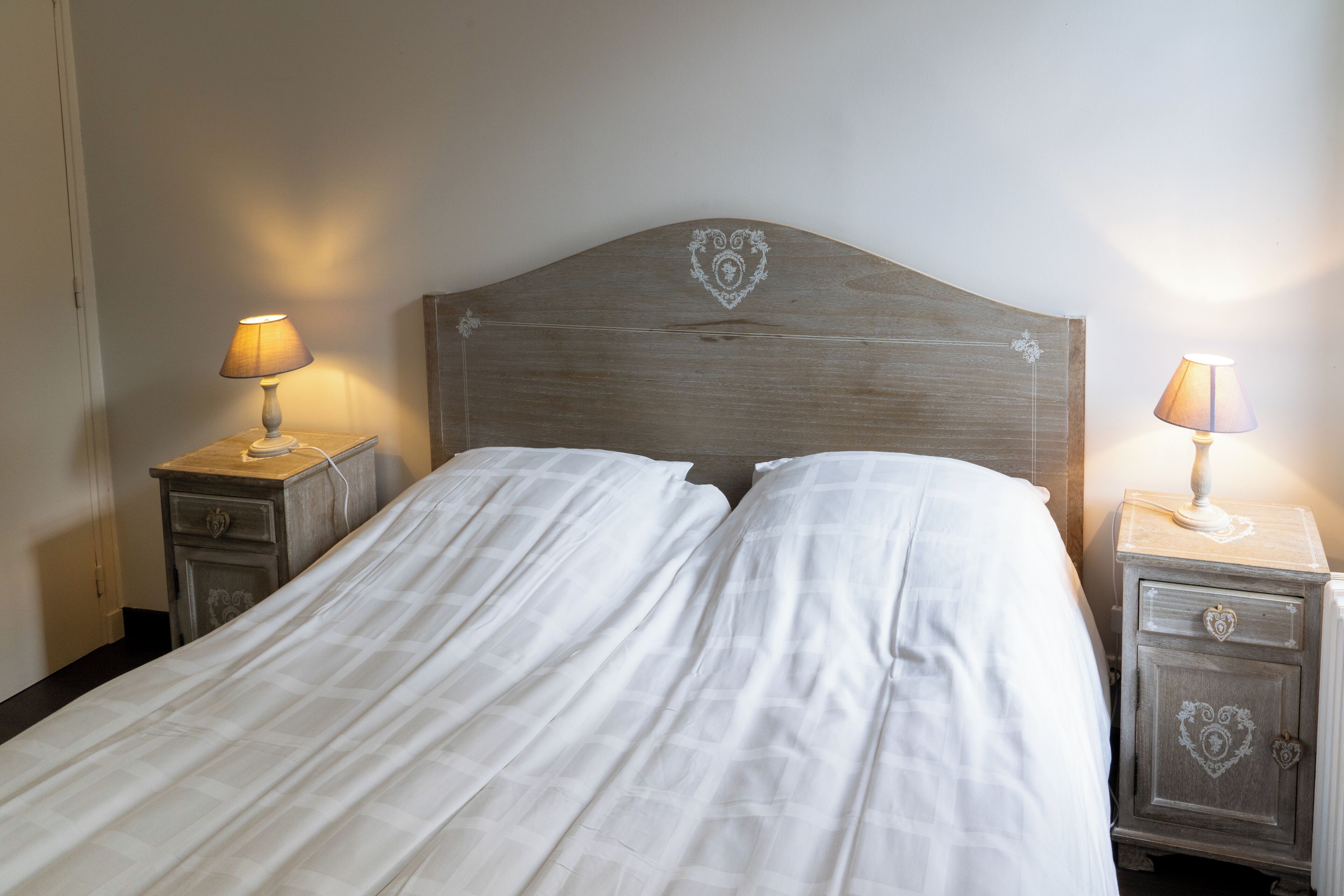 A neatly made bed with a heart-shaped headboard, two bedside tables with lamps, and a simple wall design.