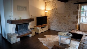 Un salon avec un mur en pierre, une cheminée, un téléviseur, une horloge et un canapé.