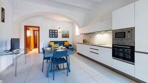 A modern kitchen with white cabinets, a dining area with blue chairs, a TV, and a microwave. - GuestHost - A comfortable and welcoming 64 square meters apartment, perfect for four people, located on the ground floor of a renovated period villa with a private entrance.The property is located in Alba Adriatica, a town famous for its long sandy beach (Alba Adriatica)