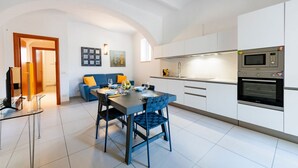 A modern kitchen with white cabinets, a built-in microwave, and an oven. There is a dining area with a table and chairs, and a blue sofa in the background. - GuestHost - A comfortable and welcoming 64 square meters apartment, perfect for four people, located on the ground floor of a renovated period villa with a private entrance.The property is located in Alba Adriatica, a town famous for its long sandy beach (Alba Adriatica)