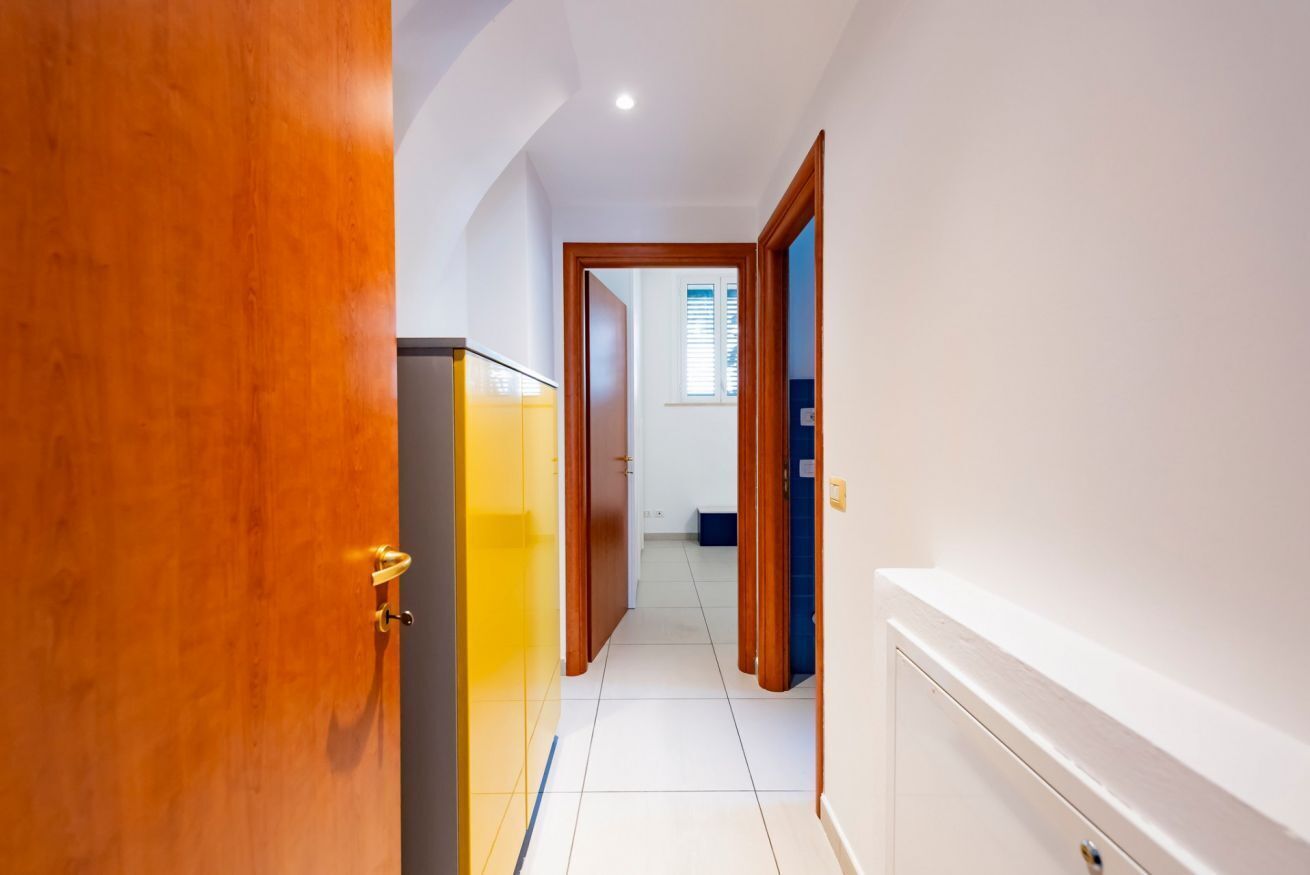 Un pasillo con puertas de madera, un refrigerador y piso de baldosas.