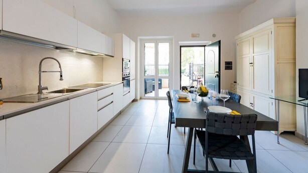 A modern kitchen with white cabinetry, a stainless steel sink, and a dining area with a table and chairs. - GuestHost - A comfortable and welcoming 64 square meters apartment, perfect for four people, located on the ground floor of a renovated period villa with a private entrance.The property is located in Alba Adriatica, a town famous for its long sandy beach (Alba Adriatica)