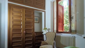 Een kamer met een houten garderobe, een stoel, een radiator en een raam met luiken.