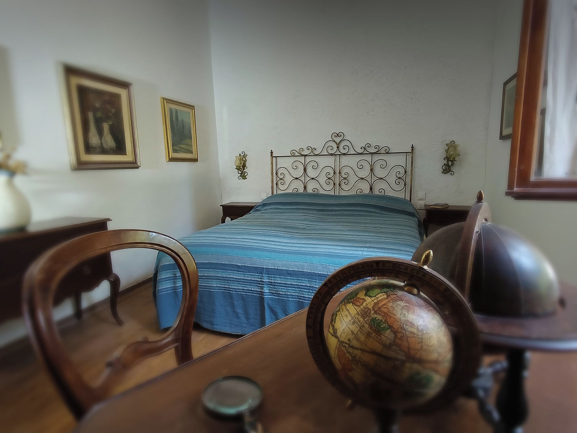 Een slaapkamer met een bed, een bureau met een wereldbol en twee ingekaderde foto’s aan de muur.