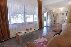 Ein Wohnzimmer mit einer Couch, einem Tisch mit Obstschale und Blick durch ein Fenster.