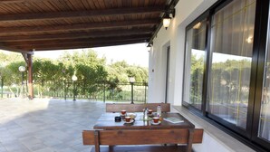 An outdoor patio with a wooden table and benches, a railing, and a view of greenery. - Apartment Near Kanegra Beach (Umag)