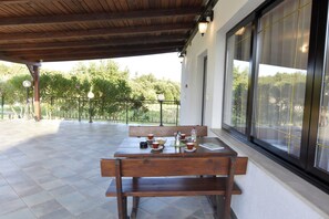 Eine Terrasse im Freien mit einem Holztisch und Bänken, einem Geländer und Blick ins Grüne.