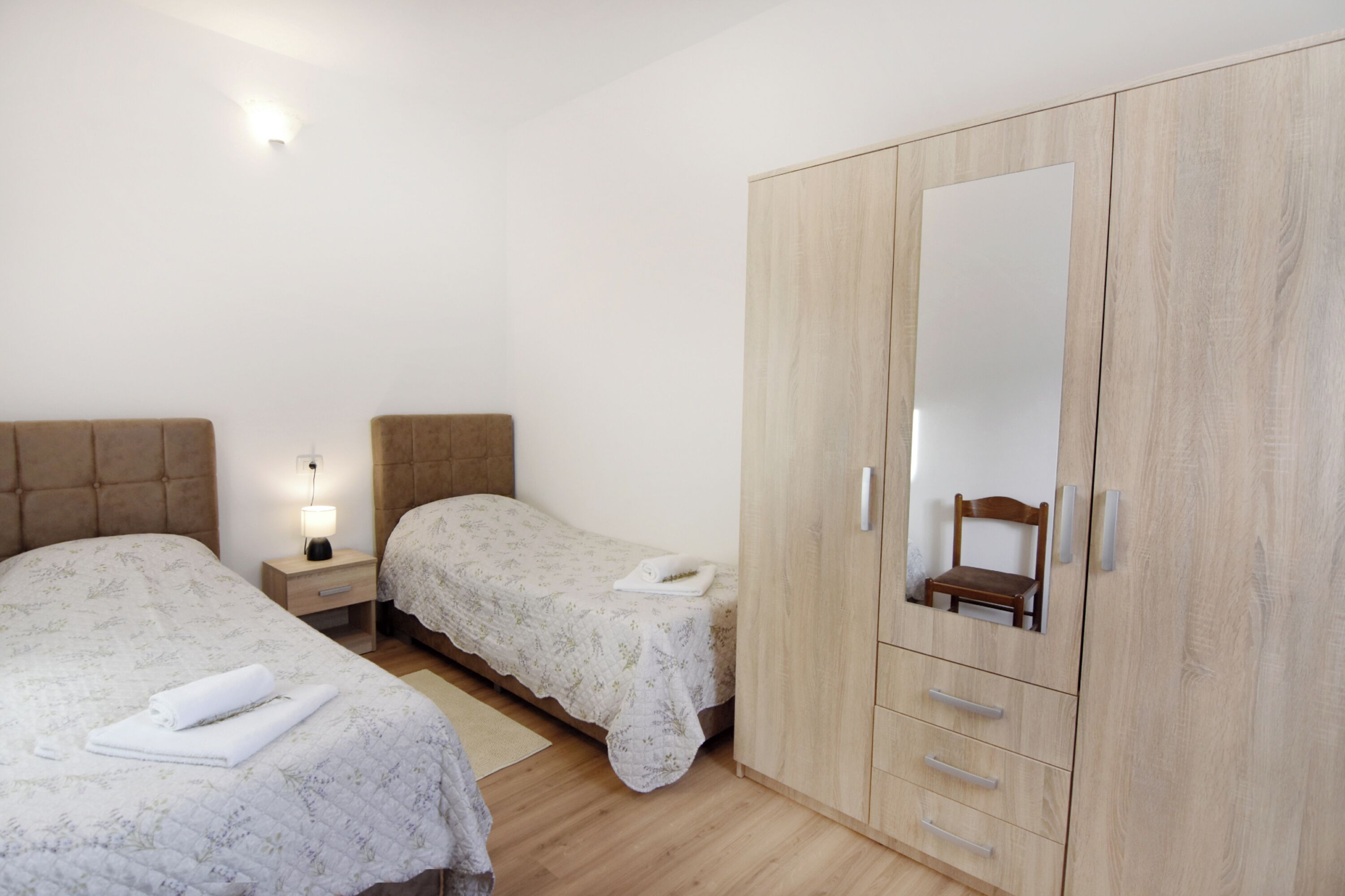 A bedroom with two beds, a wardrobe, a nightstand, and a mirror.