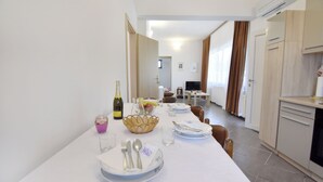 A dining area with a table set for four, a television in the background, and a kitchen area with cabinets and an oven. - Apartment Near Kanegra Beach (Umag)