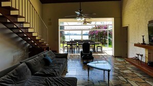 A spacious living area with a sofa, a glass coffee table, a ceiling fan, and a staircase. - House facing the reservoir, in a gated community. (São Paulo)