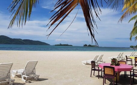 A beach with lounge chairs and a dining table, overlooking the sea and islands.