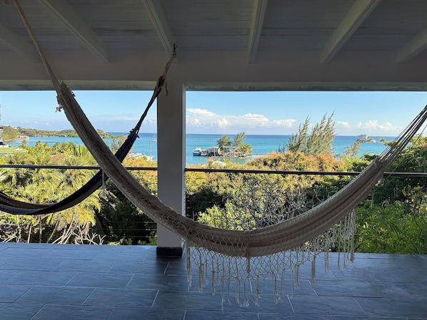 A hammock on a balcony with a view of the ocean and a small island.