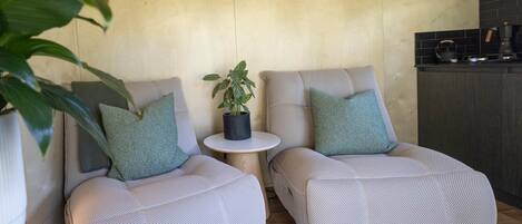 Dos sillones tapizados con estampado de espiga, una mesita redonda y una planta en maceta entre ellos.