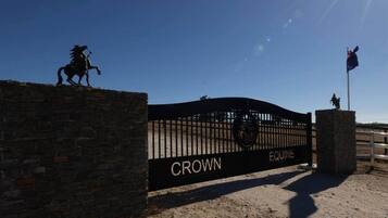 Ein verschlossenes Tor mit der Beschriftung 'CROWN EQUINE', eine Pferdestatue und eine Fahnenmasten.