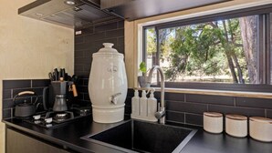 A kitchen with a black countertop, a coffee maker, a kettle, a large white water dispenser, a sink, and a window with a view of trees. - Crown Equine Retreat Under the Bridge  Romantic City Escape (North Dandalup)