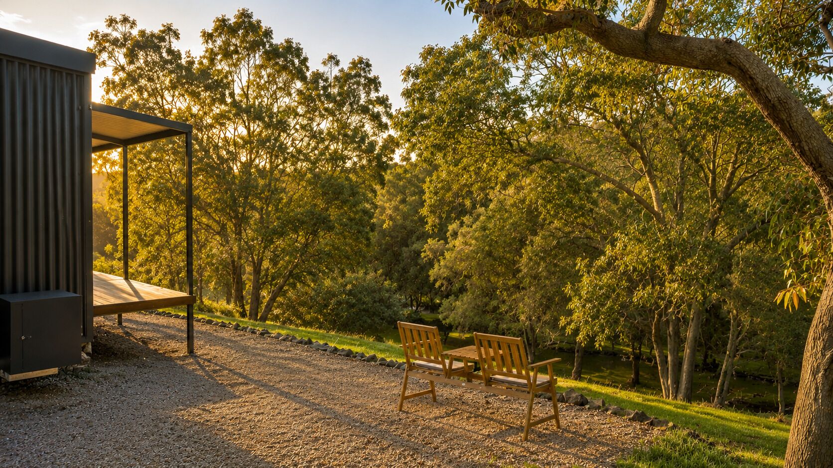 A covered outdoor seating area with two wooden benches, surrounded by trees and a gravel path.