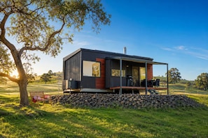 A modern cabin with a deck, large windows, and a stone foundation.