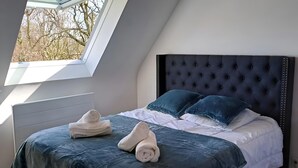 Een slaapkamer met een schuine kap, een gestoffeerd hoofdeinde en uitzicht op bomen door een dakraam.