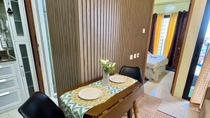A dining area with a wooden partition, a table with a lace tablecloth, two chairs, and a vase with flowers. - Elle’s Haven: A Chic & Cozy Staycation in the Heart of Cebu (Cebu City)