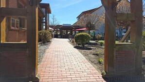 A brick pathway leading to a wooden structure with a sign, surrounded by small bushes and a clear sky. - Feriendorf an der Ostsee, Wohlenberg (Wohlenberg)