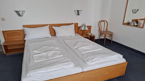 A double bed with white linens, a wooden headboard, a nightstand with a lamp, a chair, and a mirror on the wall. - Feriendorf an der Ostsee, Wohlenberg (Wohlenberg)
