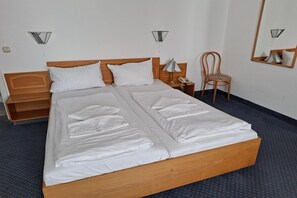 Un lit double avec du linge de lit blanc, une tête de lit en bois, une table de chevet avec une lampe, une chaise et un miroir au mur.