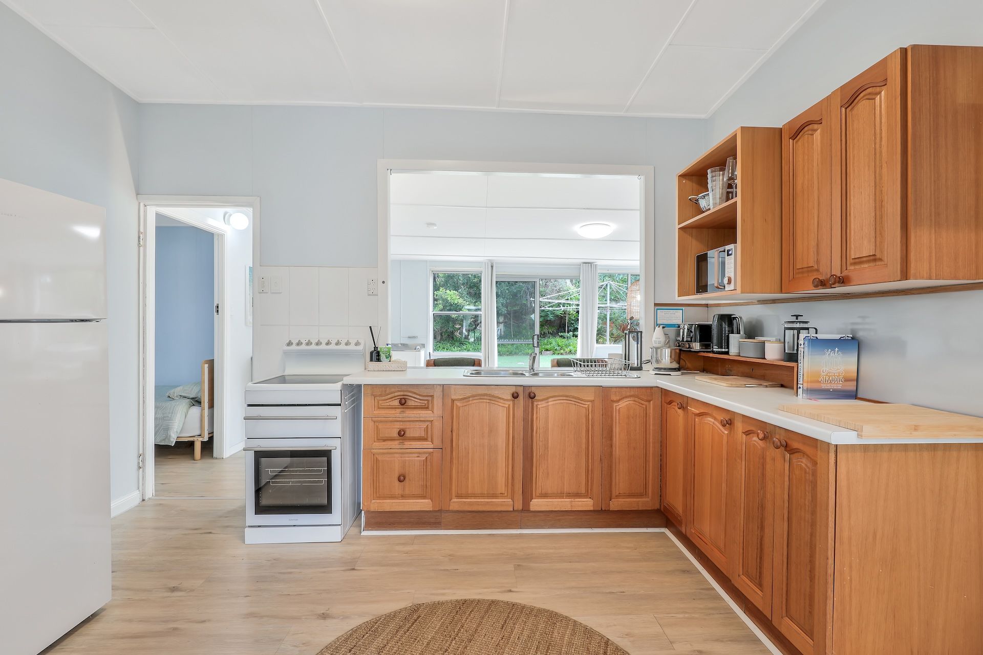 Eine moderne Küche mit Holzausstattung, einem eingebauten Backofen und einem großen Fenster mit Blick auf Grünflächen.