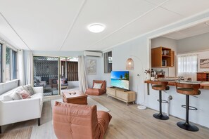 A modern living room with a sofa, chairs, a TV, and a kitchen area with bar stools. - Welcome to your classic Straddie escape in beautiful Amity (Amity)