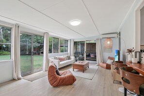 Ett rymligt vardagsrum med en vit soffa, ett träbord och en rosa sittpuff.