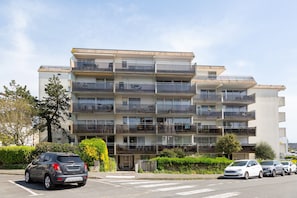Un edificio residencial de varios pisos con balcones, un área de estacionamiento y cielo despejado.