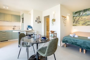A compact living space with a kitchenette, dining area, and a bed with a green bedspread. - La pause iodée – Studio with Large Balcony, Walk to Beach and Town Center (Concarneau)