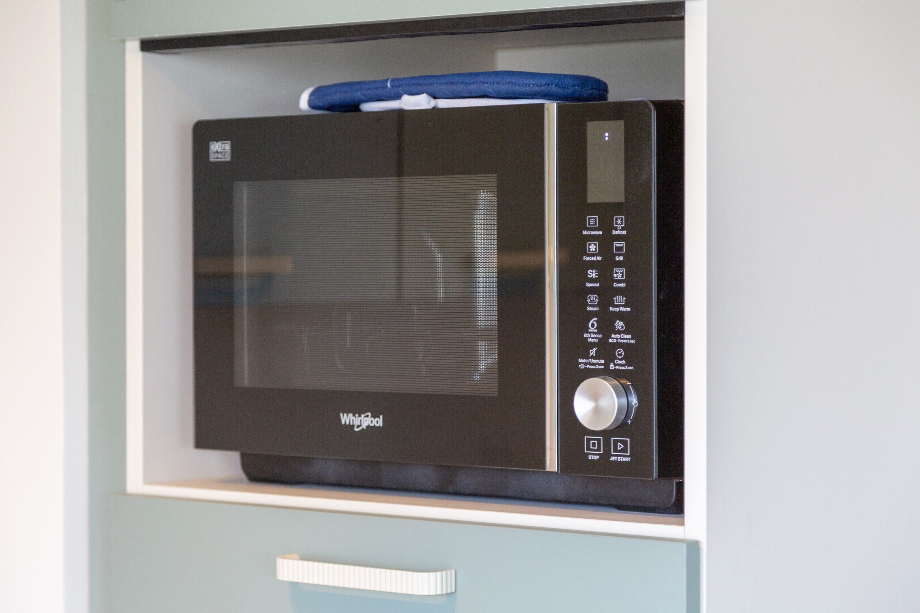 Un four à micro-ondes Whirlpool, installé dans un meuble de cuisine, est recouvert d’une housse bleue.