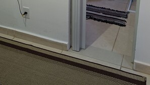Une salle de bain avec des toilettes, un petit tapis et un ventilateur fixé au mur.