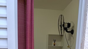 Une pièce avec une porte blanche, un rideau rouge, un ventilateur, une étagère et un tapis à rayures.