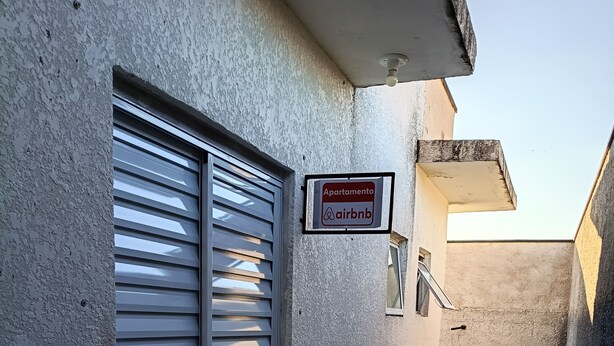 Une ruelle étroite avec une porte métallique fermée, une enseigne indiquant qu’il s’agit d’un logement Airbnb, et une petite fenêtre.